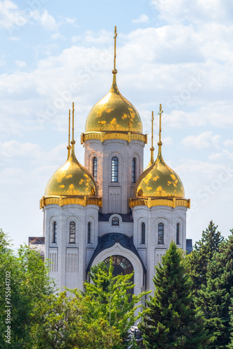 Close-up view of golden cupolas of Russian Orthodox Church of All Saints over green trees in a sunny summer day in Volgograd city, Russia. Russian culture and religion theme.