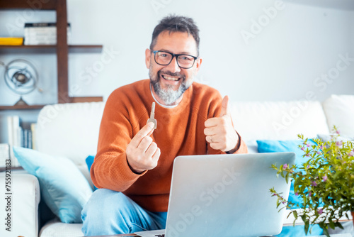 One cheerful adult man showing new hone ket and thumb up smiling at the camera. Finding house apartment online on website concept. Searching property on web. Business real estate people and notebook