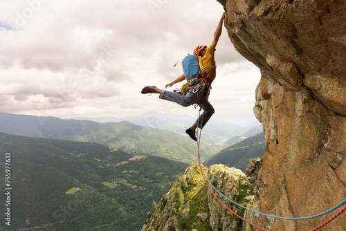 A man is climbing a rock wall with a rope. The man is wearing a yellow jacket and blue jeans. Concept of adventure and excitement