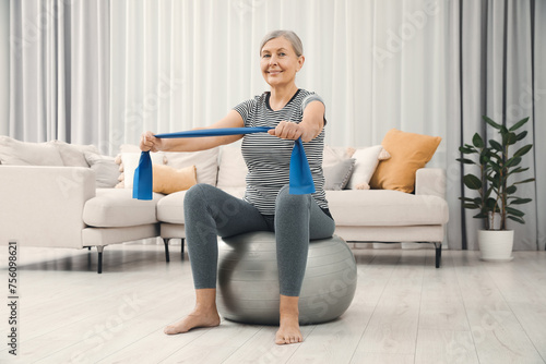 Senior woman doing exercise with elastic resistance band on fitness ball at home