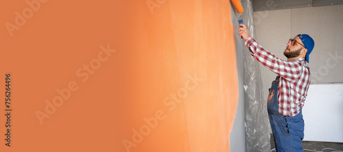 Side view of painter man painting the wall, with paint roller on big empty space. Copy space