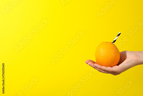 Orange with cocktail straw on hand on yellow background, space for text