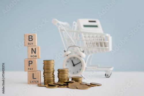 For buy now pay later , online shopping concept, wooden cube block with BNPL text and stack of coins, blurred white calculator in shopping cart and clock