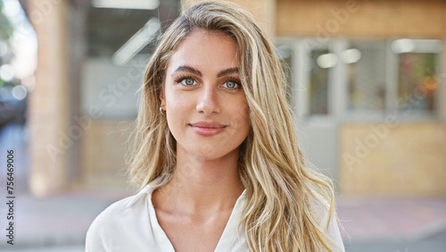 Cool, relaxed young blonde woman seriously looking at camera, standing casually in sunny urban street, attractive lifestyle portrait, outdoors with city background