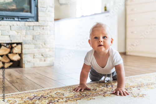 Cute little boy in a kangaroo learning to crawl on the floor in a bright living room on a rug, the child smiles, develops in early childhood