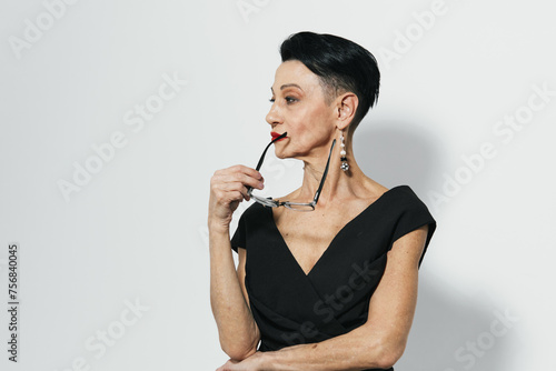 Elegant woman in black dress holding glasses, looking contemplative with chin raised, off to the side