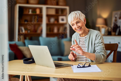 A dedicated senior adult saleswoman having a video call and negotiating with a client on a laptop at a home office