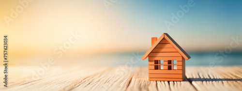 Dream home concept. Miniature wooden house model on seashore at sunrise with sky background, exuding tranquility and dreams of coastal living. Real estate investment and vacation home marketing
