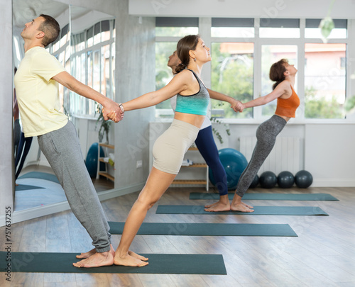 Male and female participant athletes practice pair yoga in studio during class. Lovers of active lifestyle perform doing standing deflection asana, backbend balance pose in gym