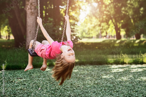 Children Holiday on Nature concept. Swing for Kids in Park. Smiling Child Having fun, Little Girl Swinging on Playground on Green Background Outside. 