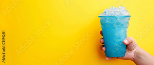 The hand holds a cup with a milk slushie. A blue glass with a coconut slushie on a yellow background, place for text