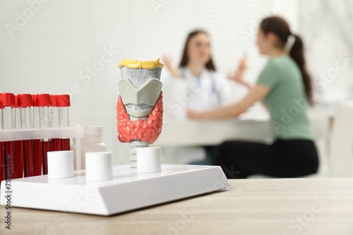 Endocrinologist examining patient at clinic, focus on model of thyroid gland and blood samples in test tubes