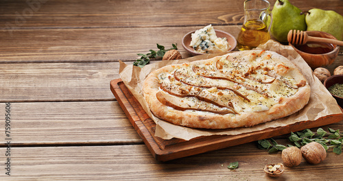 Flatbread pizza with pears, blue cheese and walnut on wooden background with ingredients for cooking. Side view, copy space. Italian food concept