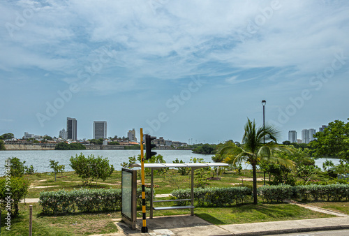 Cartagena, Colombia - July 25, 2023: Public transport stop along Transversal 17 looking over bay water on historic shore walls of old town with few tall buildings under blue cloudscape