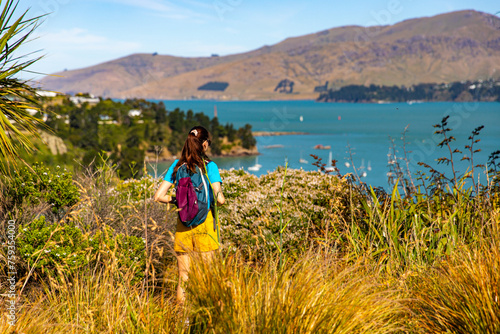 pretty backpacker girl enjoys the coastal walk between pony point and lyttelton near christchurch, canterbury, new zealand south island; hiking on the coast with the view of banks peninsula