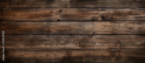 A closeup image of a wooden wall featuring brown hardwood planks with a wood stain finish. The rectangular pattern resembles brickwork, with the floor blurred in the background