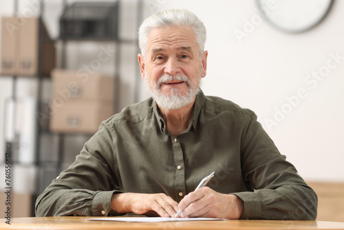 Senior man signing Last Will and Testament at table indoors