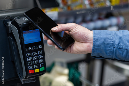Close-up of a male hand holding a smartphone to a card reader for mobile payment in a retail store setting.