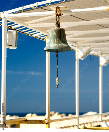 A ship's bell hanging on a sea ship against a blue sky
