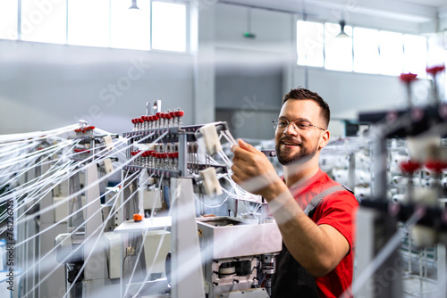 Worker preparing industrial knitting machine for work in textile factory.