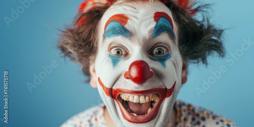 A clown with red and blue makeup on his face is smiling and laughing