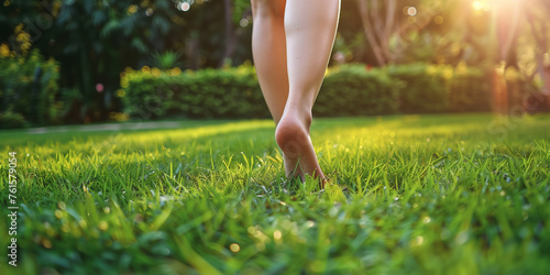 A young girl walks barefoot on the fresh green grass outdoors, closeup view. Room for text placement.