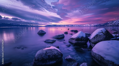 A stunning sunset illuminates a lake with snow-covered rocks in the foreground, creating a striking winter scene.