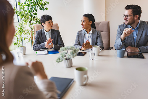 A diverse group of multi-ethnic businesswomen sit in a corporate office and have a meeting with a business associate