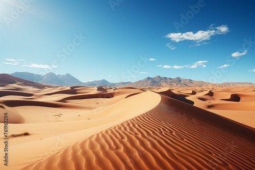 Sand dunes in the desert with mountains in the background under a clear sky