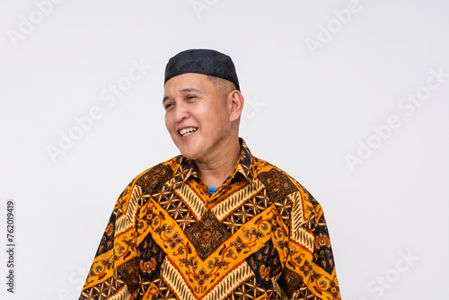 A cheerful Indonesian man wearing a patterned batik shirt and a songkok, representing traditional culture and attire.