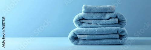 three neatly folded light blue towels stacked on blue background .banner