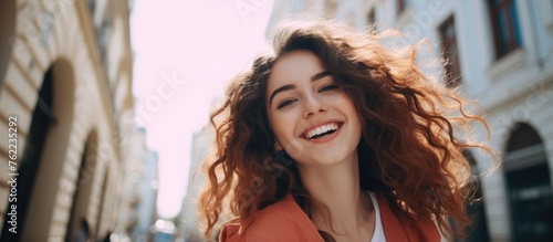 A woman with layered curly hair is laughing and smiling as she strolls down a bustling city street, clearly enjoying the vibrant atmosphere and having fun during her travel adventure