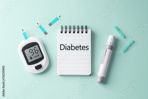Diabetes concept with notepad and blood glucose meter on light green background
