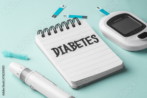Diabetes word on notepad with blood glucose sugar meter on light green background