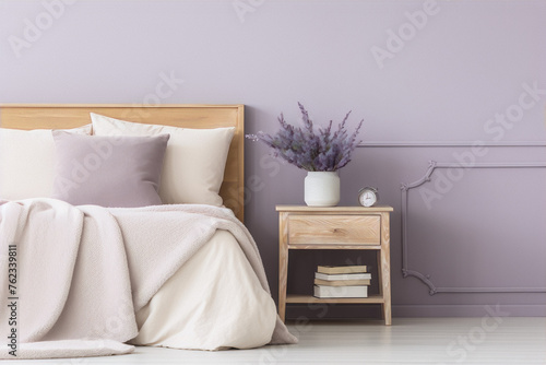 Minimalistic bedroom interior with wooden nightstand, books, lavender, alarm clock and cozy bedding.
