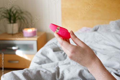 Woman in bedroom holding intimate vibrator in hand.