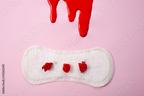 Blood and feminine hygiene pad with red flowers on pink background. First menstrual period concept 