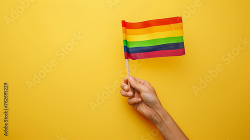 hand waiving rainbow flag against yellows color background