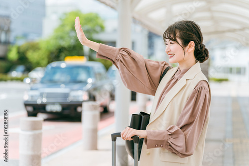 タクシー乗り場で手を挙げてタクシーを呼び止める若いアジア人ビジネスウーマン（出張・転勤） 