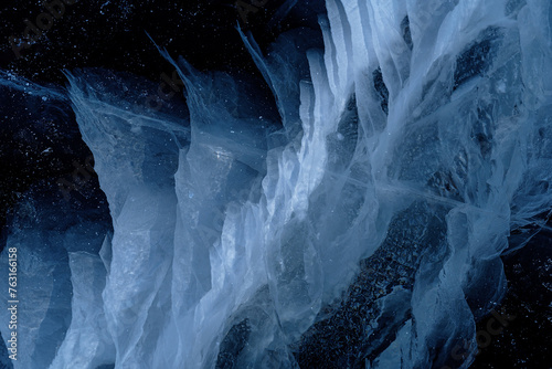 Transparent dark blue ice of frozen Baikal lake with white cracks pattern. Beautiful winter nature background.
