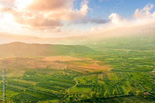 scenic rustic landscape with green hills and farms in a mountain valley during colorful cloudy sunset