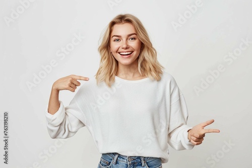 Carefree good-looking blond woman pointing upper left corner and talking to at camera with broad satisfied smile, recommend awesome place, great online store, standing on white wall joyful