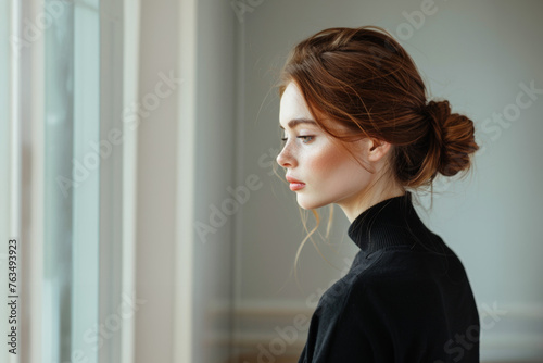 jeune femme rousse de profil cheveux attachés en chignon regardant à travers la fenêtre