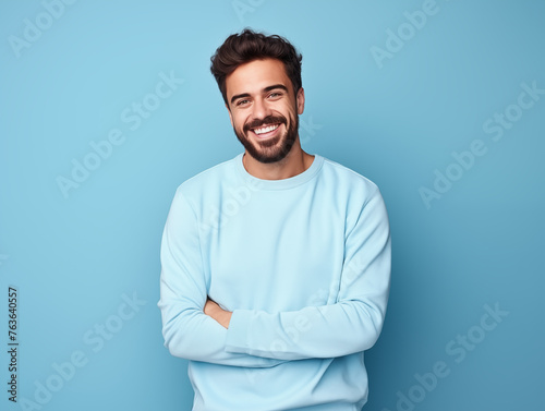 Hombre latino, joven, atractivo y con barba corta, feliz, usando ropa casual de color azul posando sobre un fondo del mismo color
