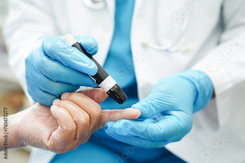Asian doctor using lancet pen on senior patient finger for check sample blood sugar level to treatment diabetes..