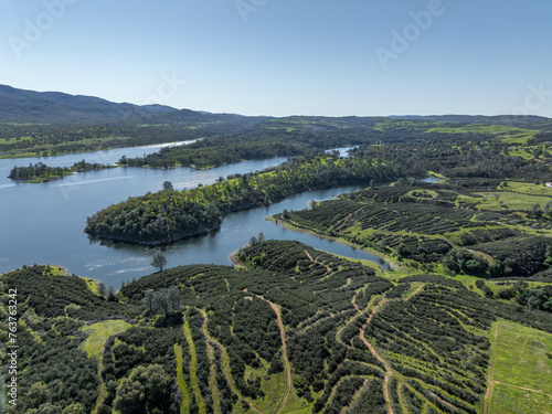 Drone image over beautiful green rolling hills in Northern California with New Hogan Lake in the background and a blue sky.