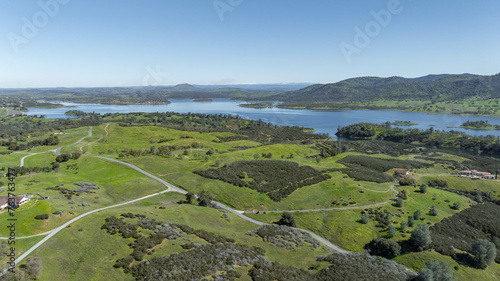 Drone image over beautiful green rolling hills in Northern California with New Hogan Lake in the background and a blue sky.