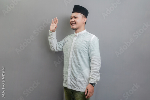 Happy asian muslim man waiving saying hello, friendly welcome gesture