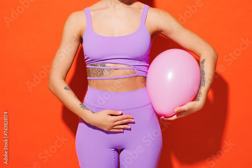 Cropped young fitness trainer instructor sporty woman sportsman wear purple top clothes in home gym hold pink balloon near belly isolated on plain orange background Workout sport fit abs diet concept