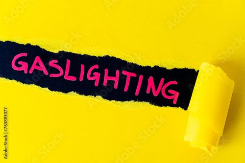 Black surface, with word gaslighting in red. Underneath torn yellow cardboard. 